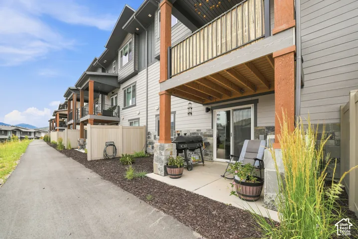 Exterior featuring horizontal lap siding, stone veneer accents, timber support posts, a covered concrete patio, and a private second-story balcony with wooden railing