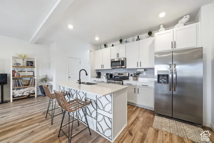 Kitchen featuring white shaker cabinetry, stainless steel appliances, quartz countertops, a decorative geometric-patterned island, and wood-finish flooring