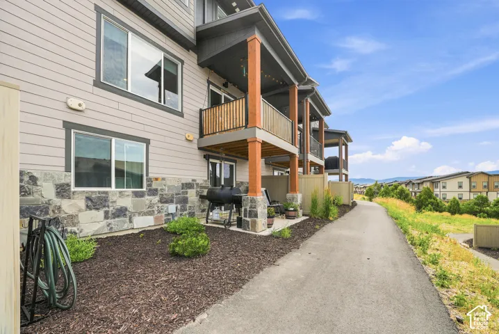 Multi-story exterior featuring horizontal siding, natural stone veneer foundation, covered balcony with wood-finish supports, and paved walkway