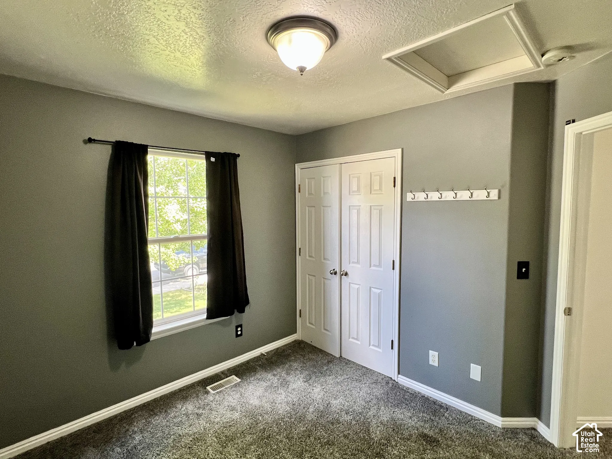 Room featuring neutral wall paint, carpeted flooring, a multi-pane window, double-panel closet doors, and wall-mounted hooks