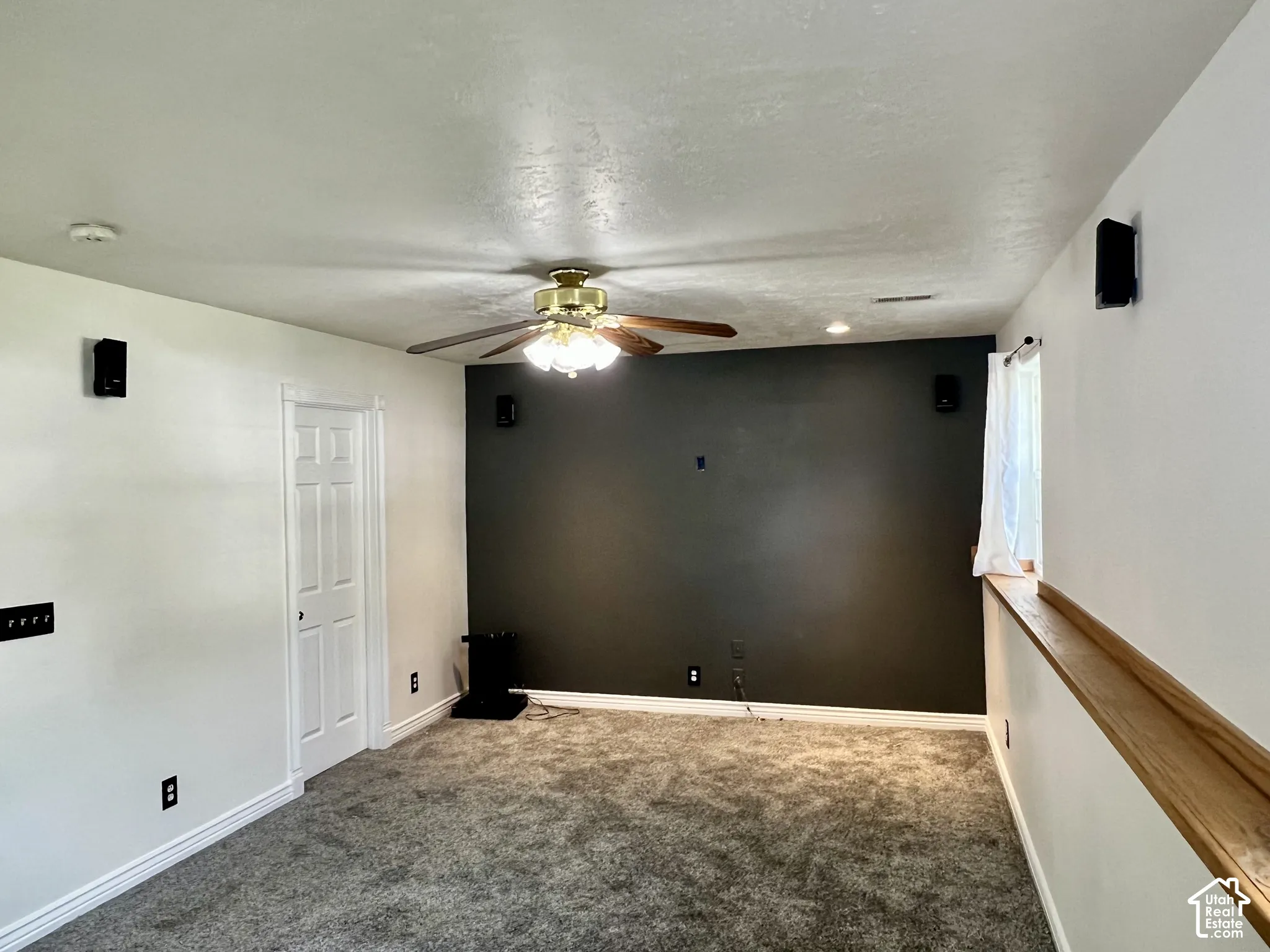 Interior room featuring a dark charcoal accent wall, neutral carpeting, ceiling fan with light fixture, six-panel door, and a built-in wood-finish window ledge