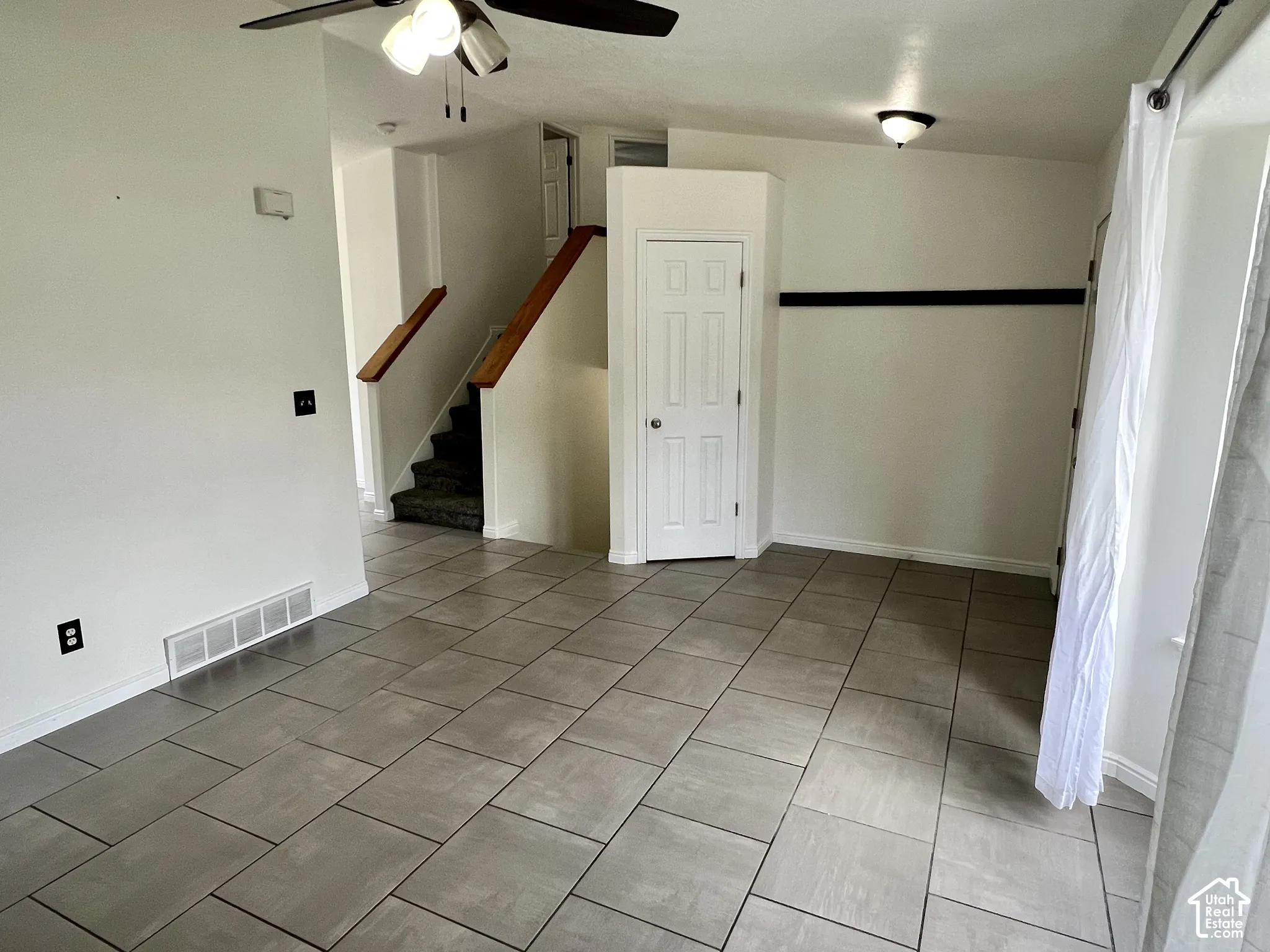 Neutral-toned tile flooring, recessed and ceiling-mounted light fixtures, and a staircase featuring wood-finish handrails