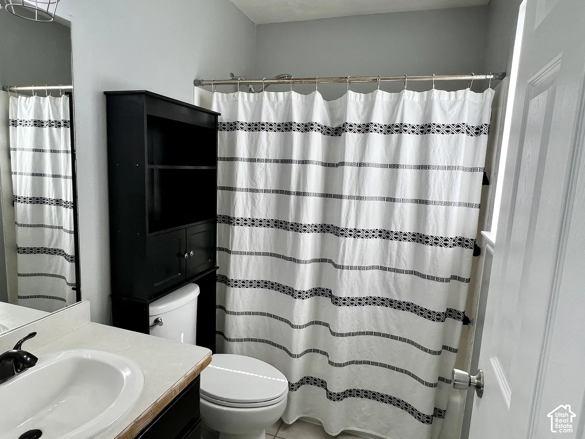 Bathroom featuring a vanity with integrated sink, faucet with curved spout, wall-mounted mirror, and an over-the-toilet storage unit
