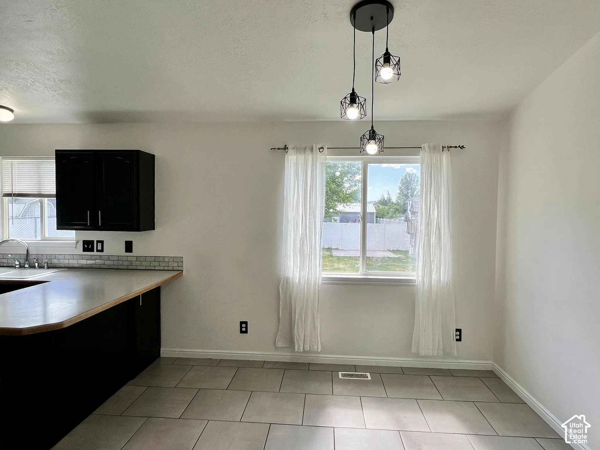 Kitchen area featuring dark-toned cabinetry, tile flooring, a multi-light pendant fixture, and a neutral tile backsplash