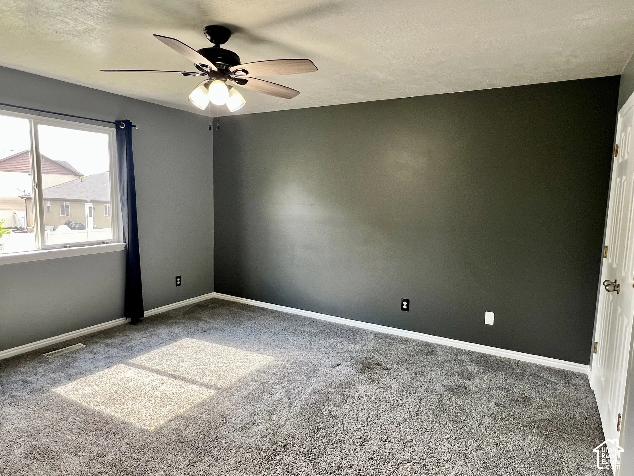 Neutral-toned carpeting, dark-finished accent wall, multi-blade ceiling fan with integrated lighting, and white multi-panel interior door