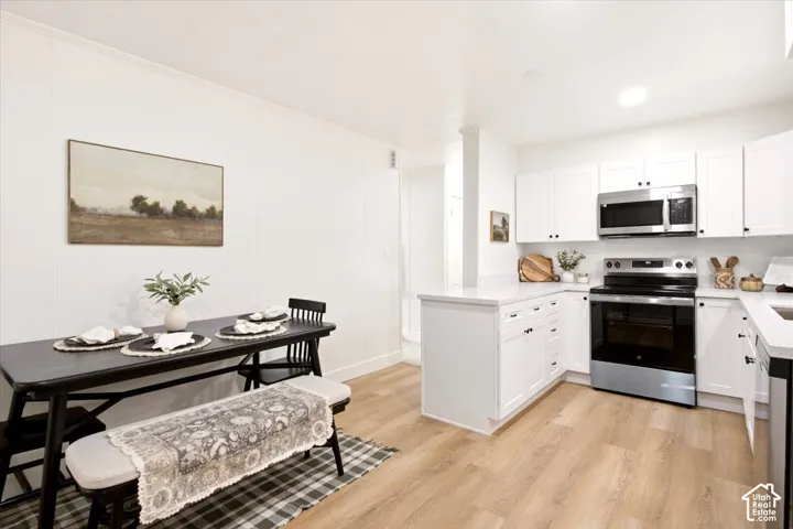 Kitchen featuring white cabinetry, solid-surface countertops, wood-finish flooring, and built-in stainless steel appliances including an over-the-range microwave and electric range