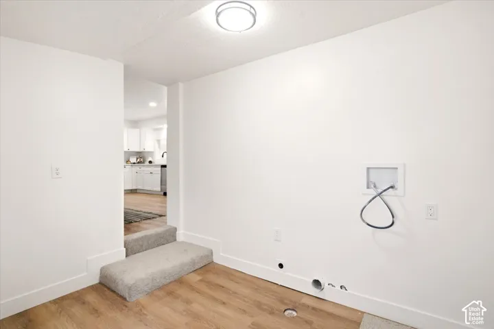 Laundry area featuring wood-finish flooring, a recessed water supply box, and a flush-mount ceiling light fixture
