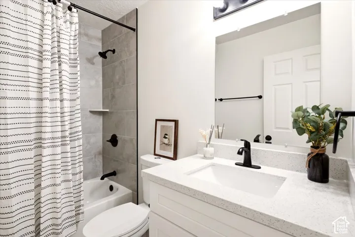Bathroom featuring a white vanity with a speckled countertop, integrated rectangular sink, matte black faucet, and a shower-tub combination with grey tile surround