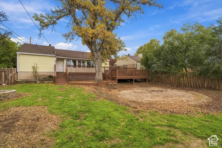 Backyard featuring a raised wooden deck, partial wood fencing, a stone-block fire pit, and mature trees