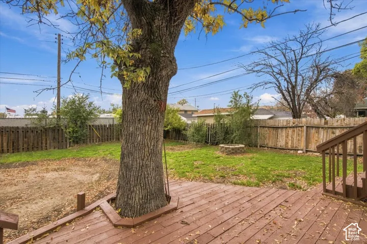 Backyard featuring a wood-finish deck with a built-in tree surround, natural grass lawn, stone fire pit, and full wood perimeter fencing