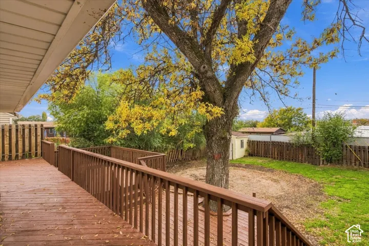 Elevated wood deck with balustrades, fenced backyard, and mature trees