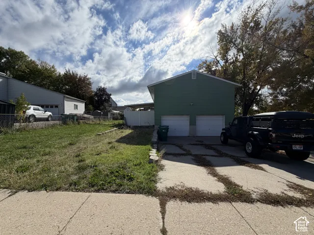 Two-car garage featuring dual overhead doors, concrete driveway, and side-yard lawn space
