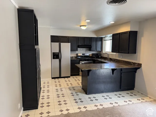 Kitchen featuring dark cabinetry, stone-finish countertops, an integrated peninsula, a patterned tile floor, and stainless steel appliances