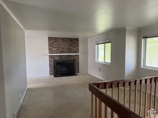 Living area featuring a floor-to-ceiling brick fireplace with a wood mantel, carpeted flooring, and a wood-slat railing