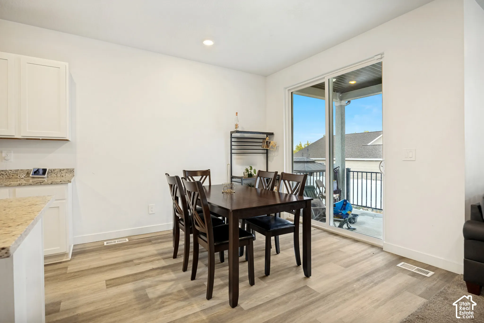 Neutral-toned wood-finish flooring, white cabinetry, speckled stone-surface countertops, and a sliding glass door opening to a covered balcony with metal railing