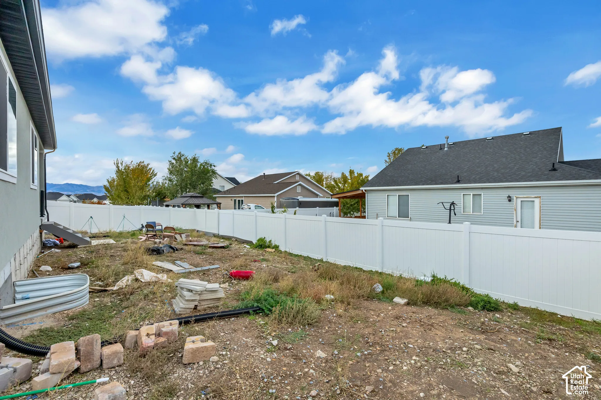 Backyard featuring a full-height white vinyl privacy fence, metal window well cover, and mountain background