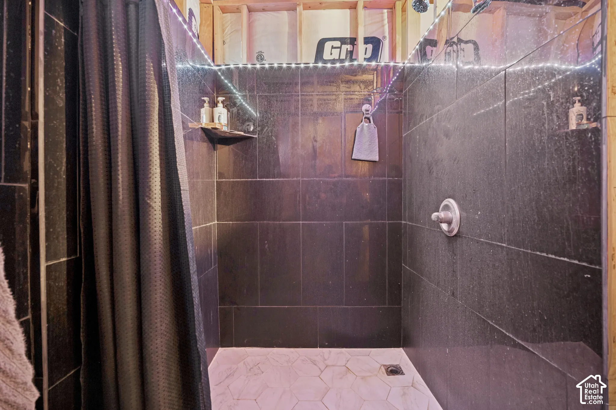 Shower enclosure featuring dark rectangular wall tile, hexagonal floor tile, and a circular pressure-balance valve