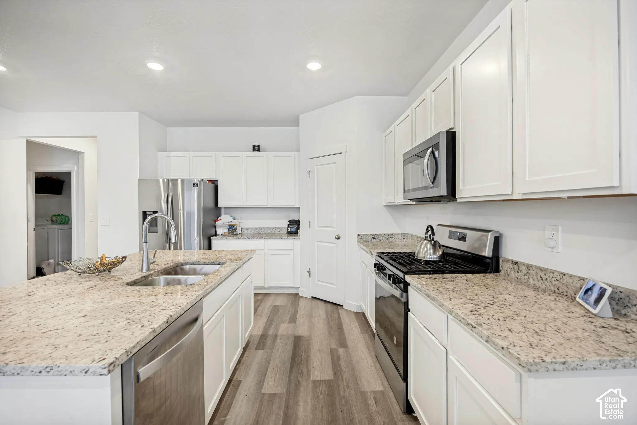 Kitchen featuring white cabinetry, stone-surface countertops, wood-finish flooring, and stainless steel appliances