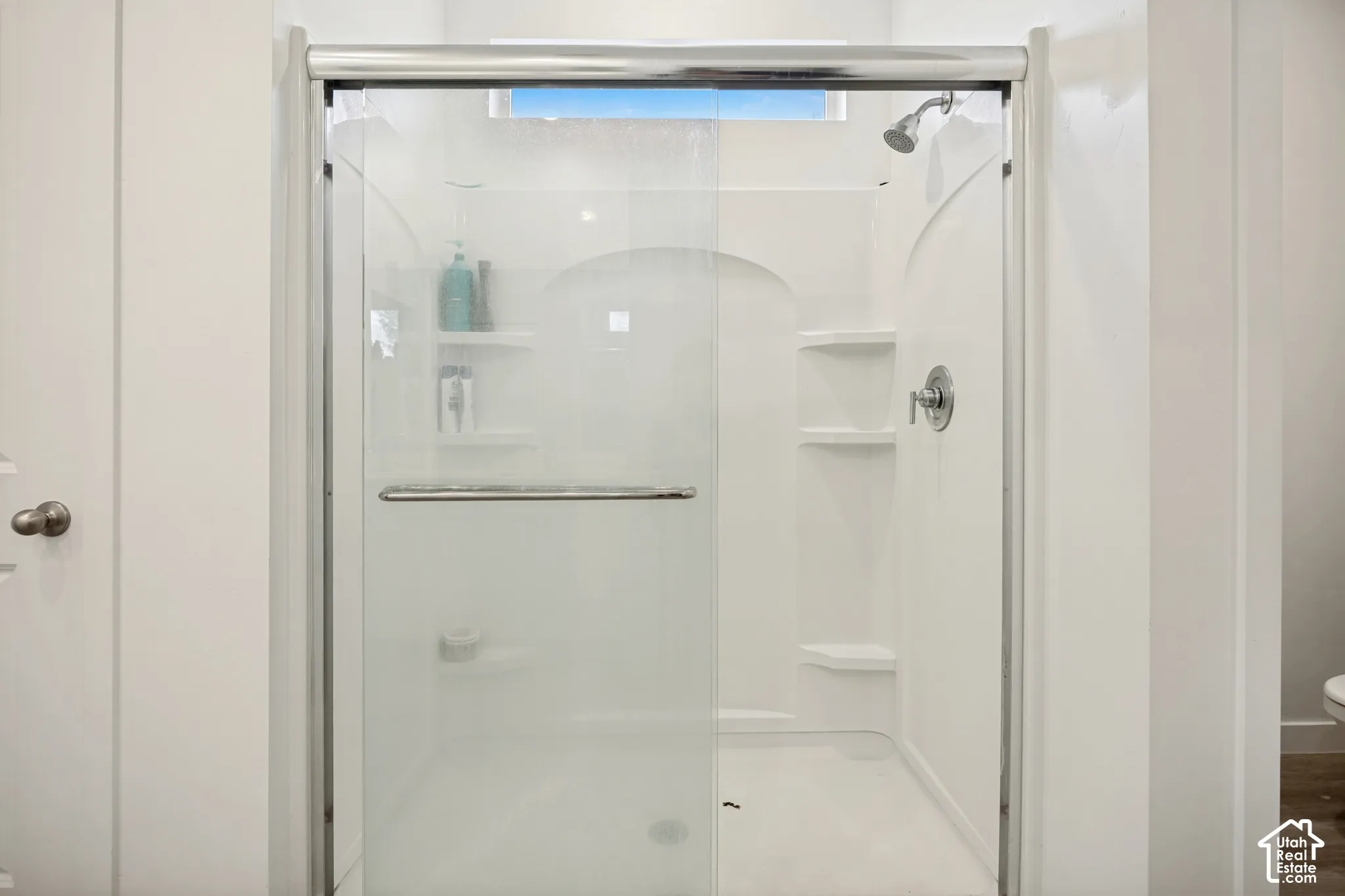 Walk-in shower enclosure featuring a sliding glass door, integrated shelving, polished chrome hardware, and a transom window