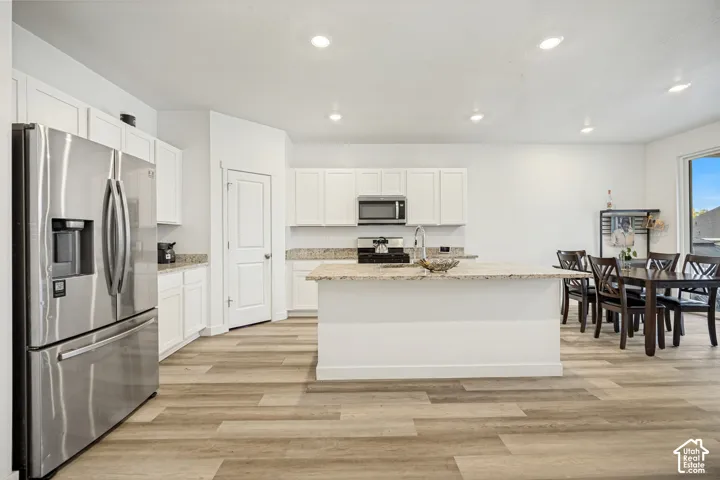 Kitchen featuring white shaker-style cabinetry, stone-surface countertops, central island, stainless steel appliances, and wood-finish flooring