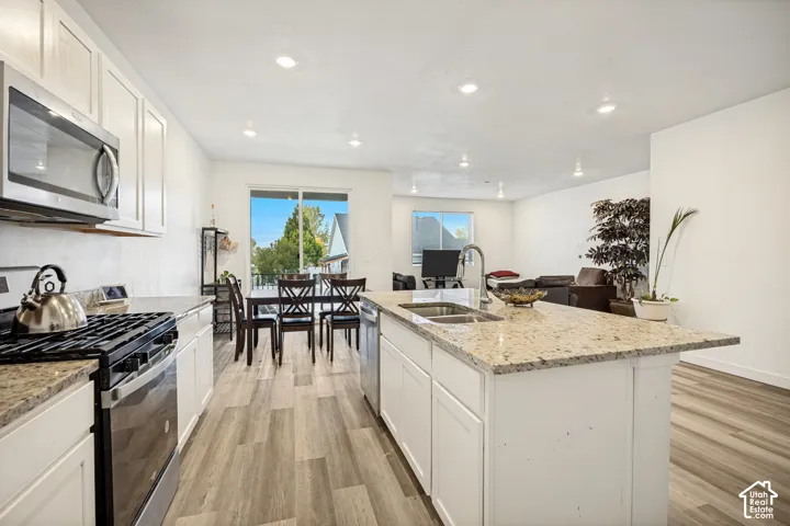Kitchen featuring stone countertops, white cabinetry, stainless steel appliances, a center island with a dual-basin sink, and wood-finish flooring