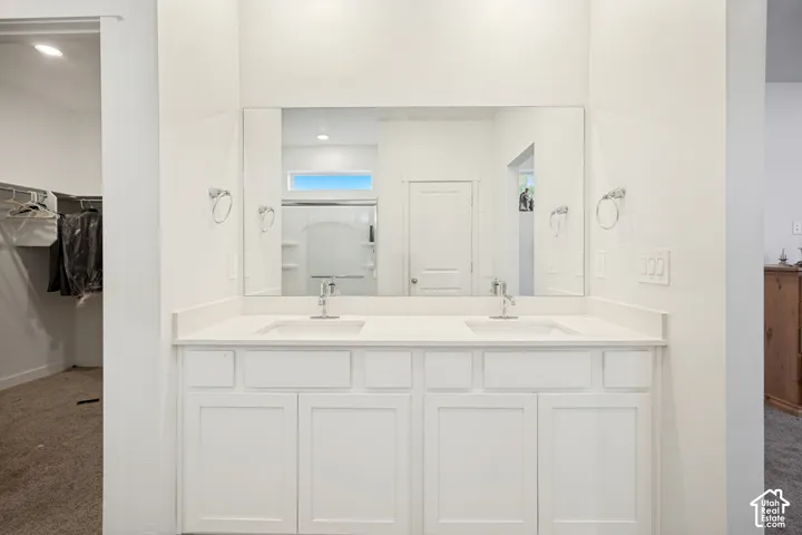 Double vanity featuring white shaker-style cabinetry, solid-surface countertops, integrated dual sinks, and a large frameless mirror