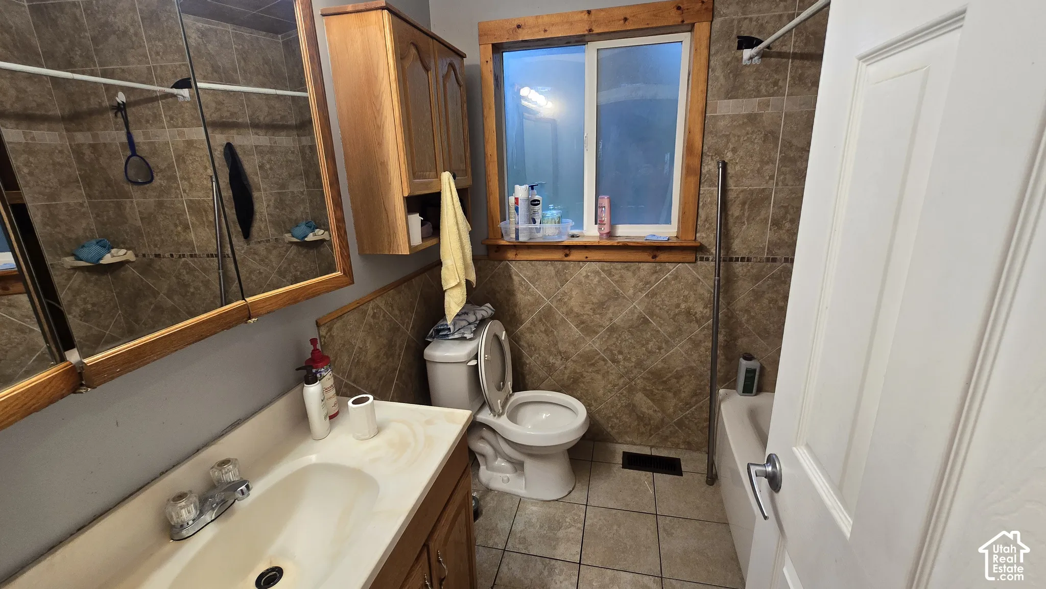 Bathroom featuring tile flooring, stone-tiled wall surrounds, a wood-framed medicine cabinet, a built-in wood vanity, and a sliding glass window