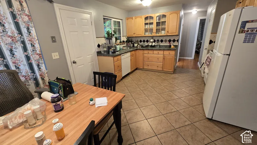 Kitchen featuring light-finish cabinetry with glass-panel upper doors, patterned ceramic tile backsplash, stone-finish countertops, and ceramic tile flooring