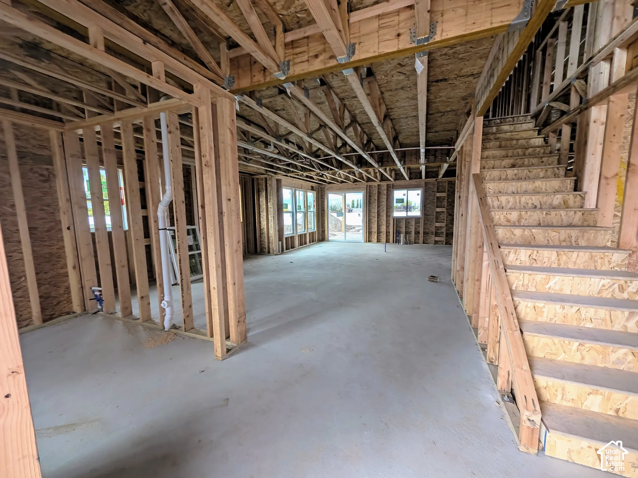 Structural wood framing featuring exposed trusses, engineered wood stair system, concrete slab foundation, and installed windows