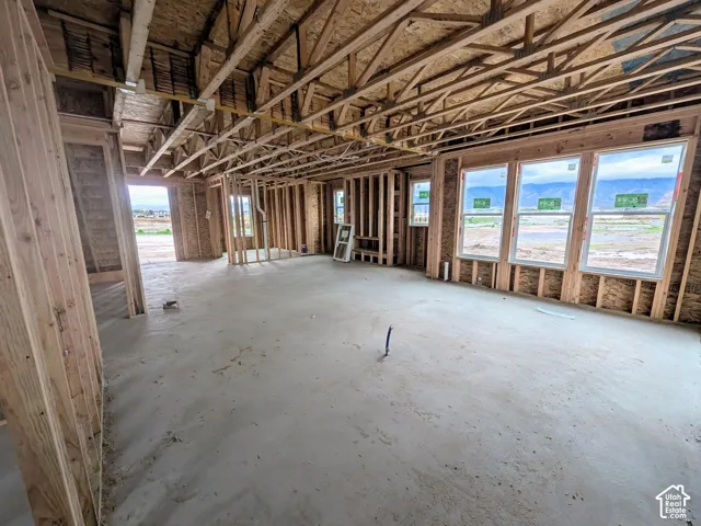 Interior framing featuring exposed wood stud walls, open-truss ceiling rafters, concrete slab flooring, and triple-pane window installations with mountain silhouettes