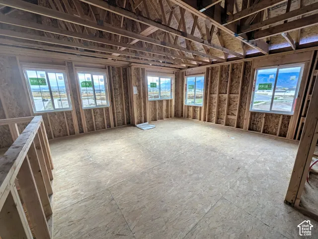 Unfinished interior featuring exposed wood-frame wall construction, exposed truss ceiling, subflooring, and multiple windows with mountain backdrops