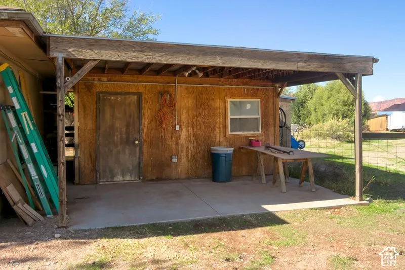 Covered carport with outdoor workspace featuring a concrete slab foundation, exposed beam ceiling construction, and exterior-grade plywood wall paneling