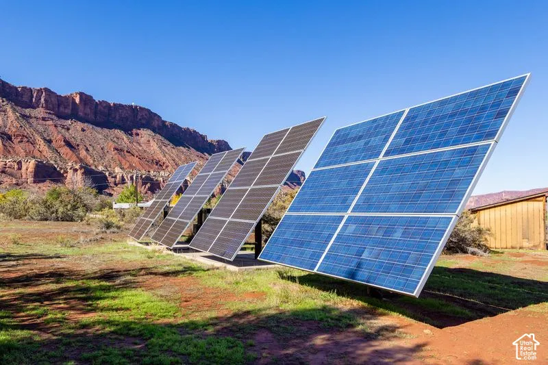 Ground-mounted solar panel array situated on natural desert landscape with rock formation backdrop