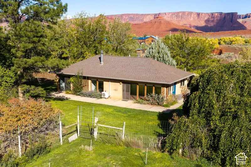 Single-story residence featuring a hipped roof, concrete patio, exterior lattice detail, and metal fencing, set against a backdrop of red rock bluffs