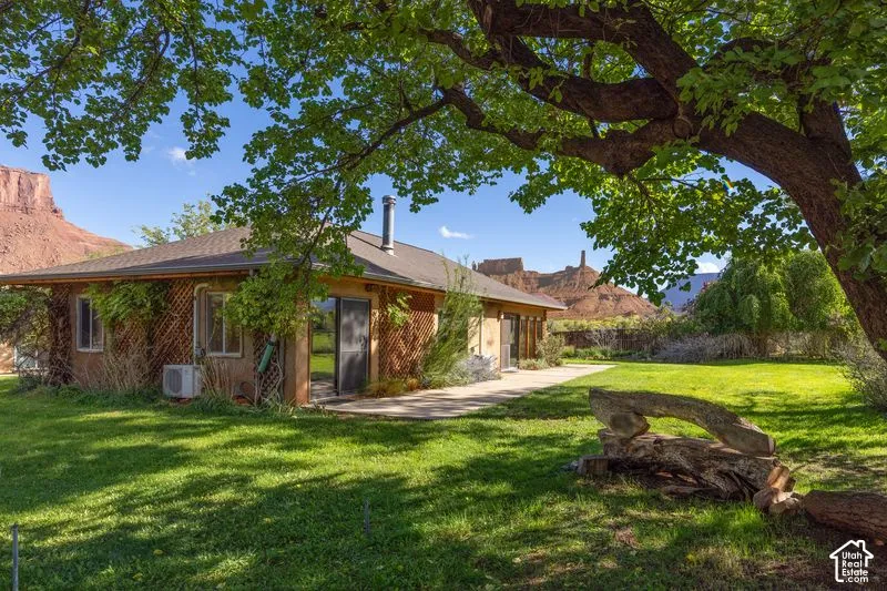 Single-story exterior featuring a concrete patio, lattice detailing, hip roof, and large sliding glass doors, set against a backdrop of prominent rock formations and mature tree canopy