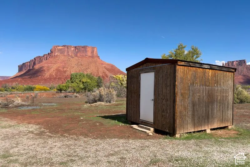 Wood-sided storage structure with a metal roof and solid-core door, set on expansive grounds featuring red rock mesa scenery