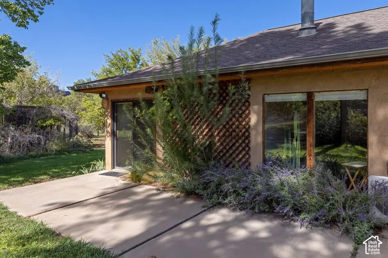 Concrete patio area featuring stucco siding, decorative wood lattice screening, sliding glass doors, and large windows