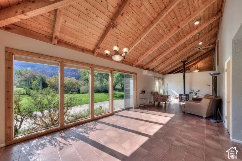 Vaulted wood-plank ceiling with exposed rafters, floor-to-ceiling windows, tile flooring, and a freestanding wood-burning stove