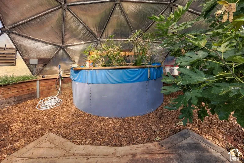 Geodesic greenhouse featuring a metal frame, mulch flooring, wood-paneled walls, and a large circular water containment system with Gold Fish.