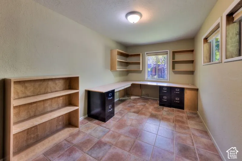 Room featuring tiled flooring, built-in wooden shelving, a large L-shaped wooden desk with integrated cabinetry, and a flush-mount light fixture