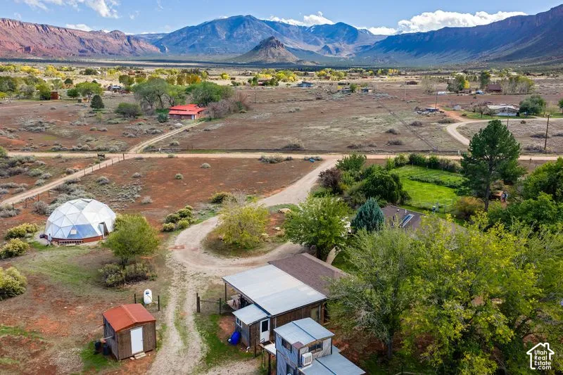 Aerial perspective featuring a geodesic dome structure, multi-level outbuilding with metal roofing, mature trees, and extensive desert landscape against a mountain backdrop