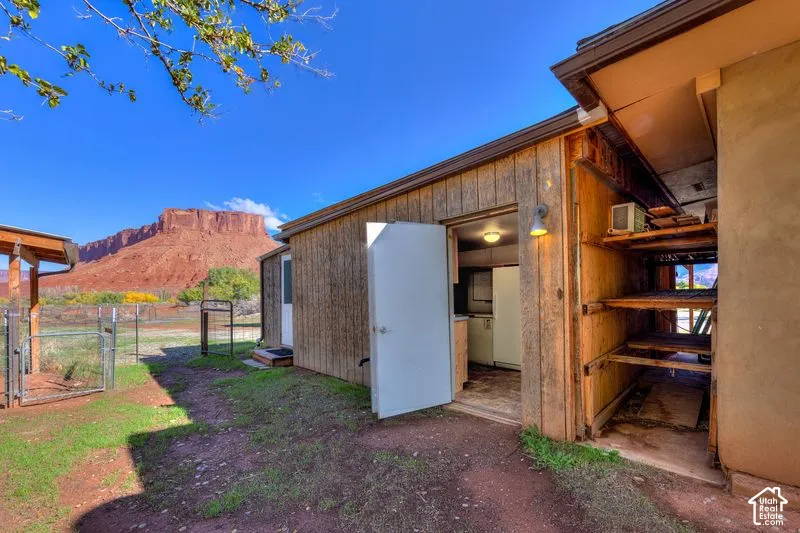 Exterior structure featuring wood-panel siding, an open-frame storage area with built-in shelving, an external light fixture, and a scenic mountain backdrop