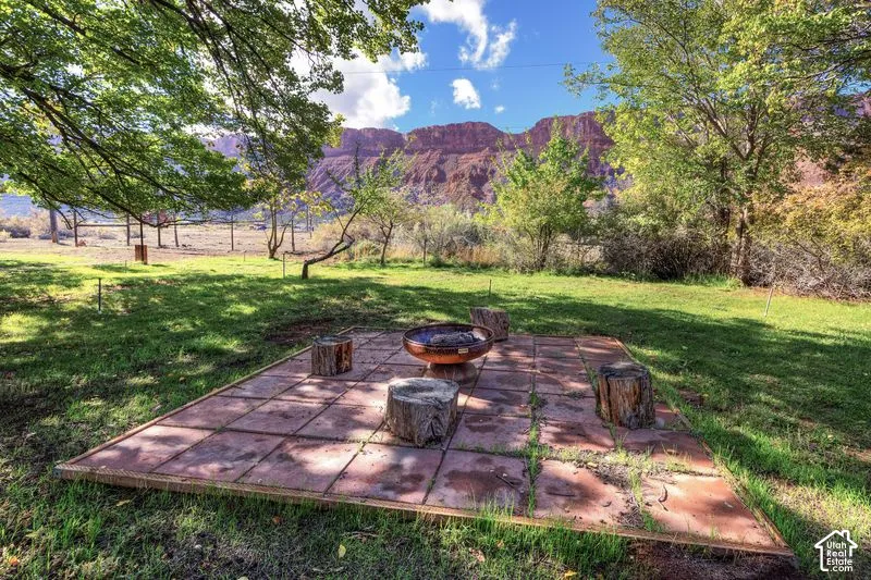 Square masonry paver patio featuring a metallic fire feature and expansive natural scenery with prominent red rock formations and mature trees