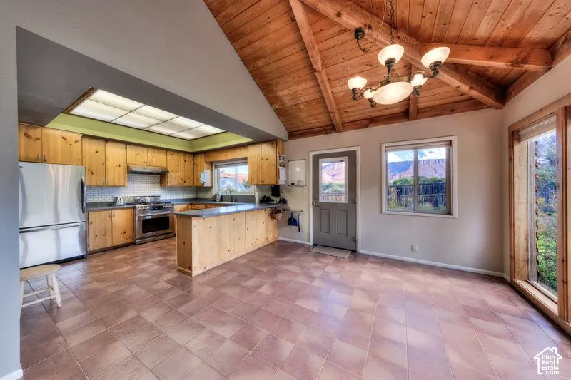 Kitchen featuring natural wood cabinetry, stainless steel appliances, tile flooring, and a vaulted ceiling with exposed wood beams and a multi-arm chandelier