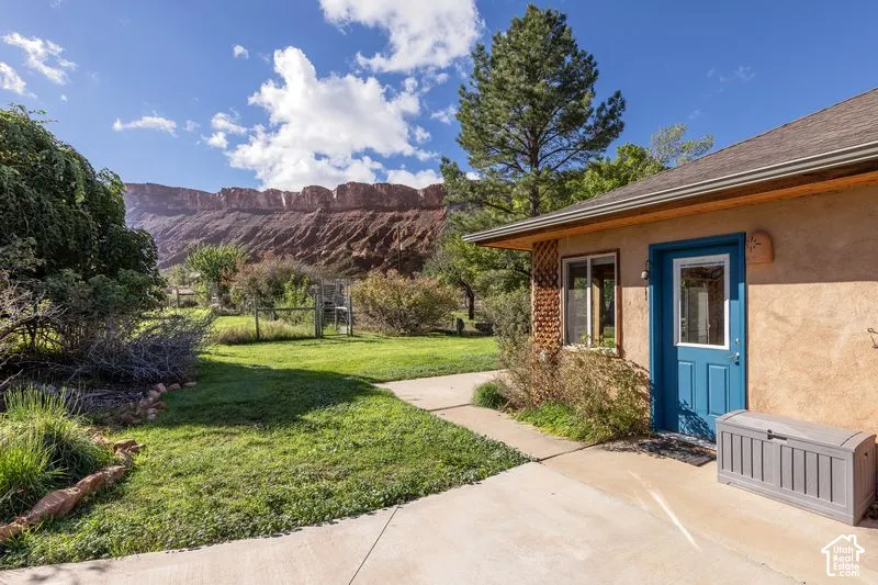 Exterior grounds featuring a concrete patio, grassy lawn, mature trees, and a desert mesa backdrop