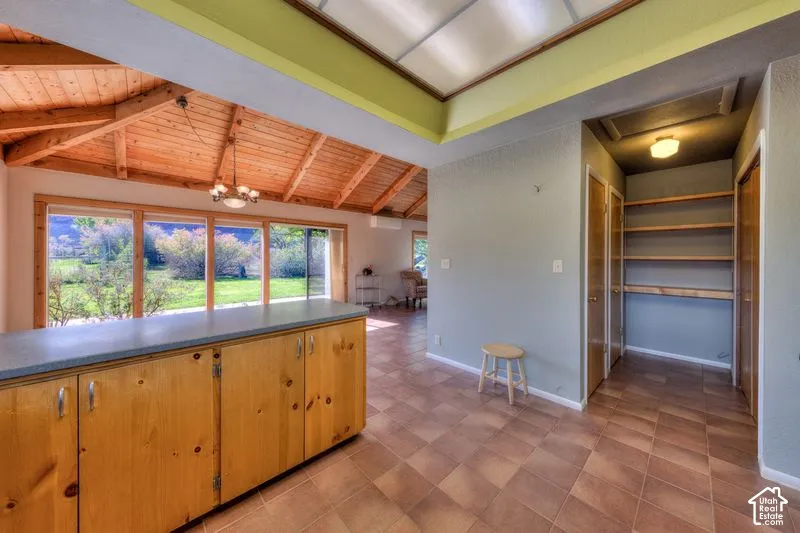 Vaulted timber-plank ceiling, kitchen island with solid-surface countertop, floor-to-ceiling windows, and integrated wall shelving