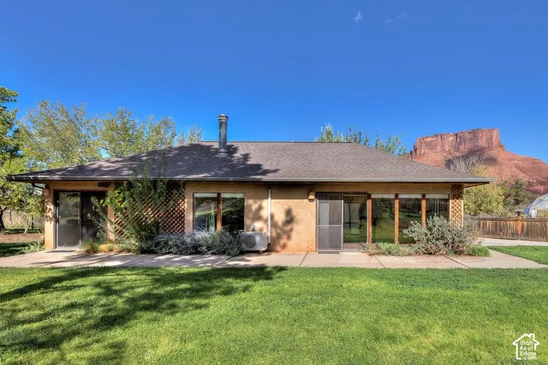 Exterior elevation featuring stucco siding, integrated lattice screening, concrete patio, and a backdrop of prominent rock formations