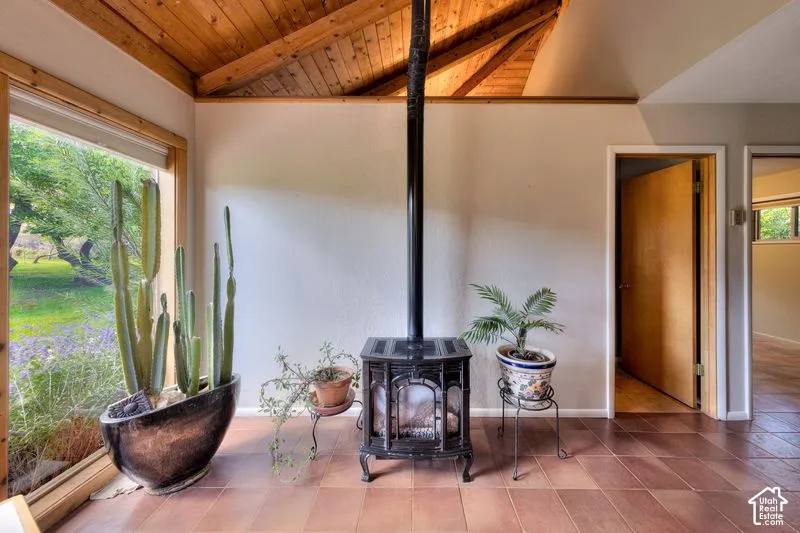 Vaulted ceiling with exposed wood-finish beams, freestanding cast-iron stove, large window, and tile flooring