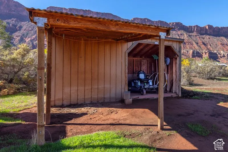 Covered outdoor storage structure with vertical wood siding, exposed timber framing, and a corrugated metal roof, set against a backdrop of prominent rock formations