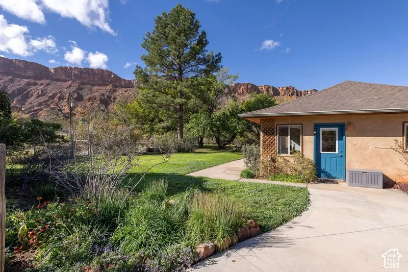 Stucco exterior featuring a concrete walkway, established landscaping, and mountain backdrop